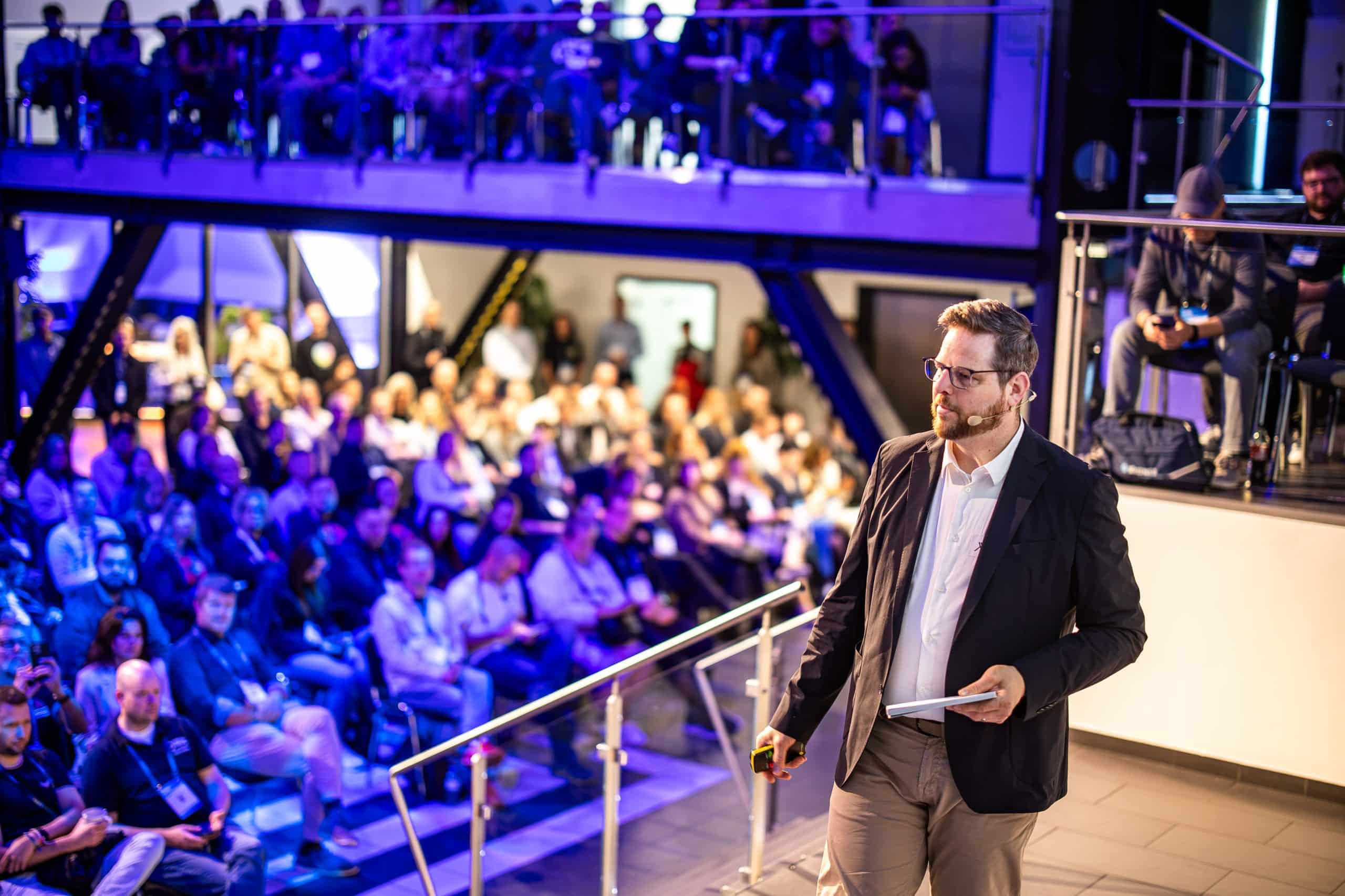 Kai Spriestersbach mit Headset vor dem Publikum bei seiner OMT-Keynote 2026.