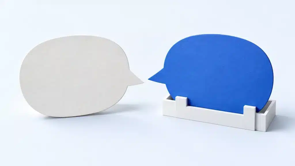 Weiße und blaue Sprechblase aus Karton auf hellem Hintergrund. Die blaue Sprechblase steckt in einer weißen Halterung.